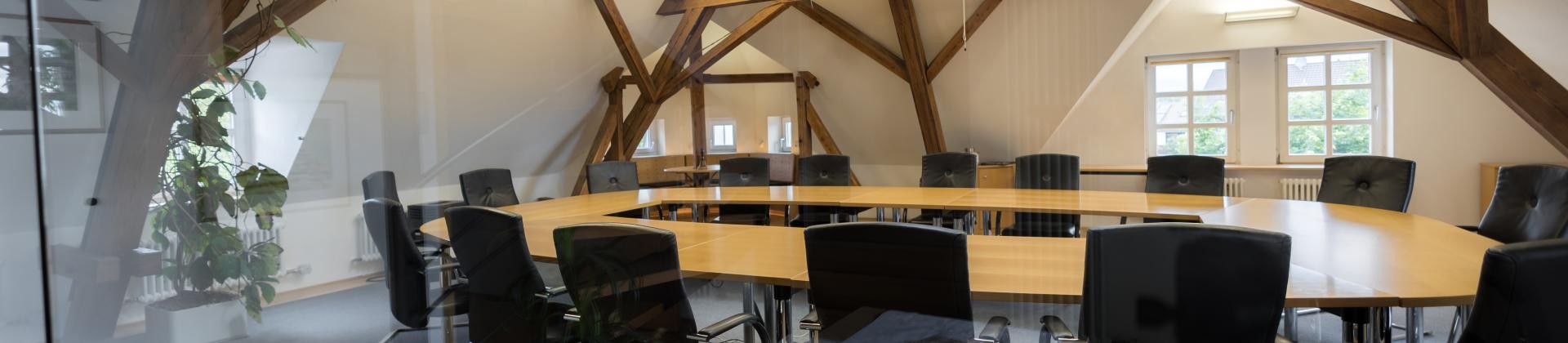 Sitzungssaal (Bürgersaal) der Gemeinde Dauchingen. Schwarze Schwingstühle an einem Konferenztisch aus Holz umgeben von Holzbalken.