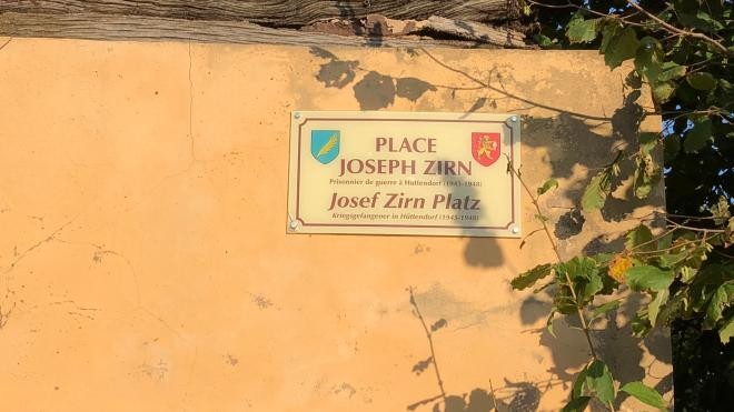 Bild zeigt ein Schild auf einer Hauswand, es sind die Wappen der Gemeinde Hüttendorf und Dauchingen zu sehen aund es steht "Place Josep Zirn" gesgeschrieben.