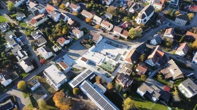 Der neu angelegte Dorfplatz aus der Vogelperspektive umgeben von Wohnhäusern und öffentlichen Gebäuden.