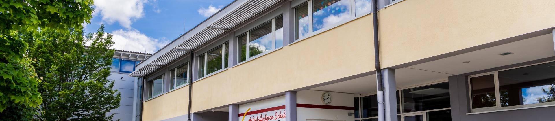 Die Astrid-Lindgren-Schule vom Schulhof aus fotografiert. Ein Flachdachgebäude mit gelb-grauem Anstrich.