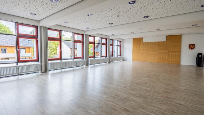 Der Innenraum des Florianssaals mit einem hellen Boden in Holzoptik und seinen roten Fenstern bei Tageslicht. Der Innenraum des Florianssaals mit einem hellen Boden in Holzoptik und seinen roten Fenstern bei Tageslicht.