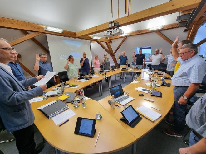 Am runden Ratstisch stehen die Gemeinderäte und halten Ihre Hand für den Schwur nach oben.