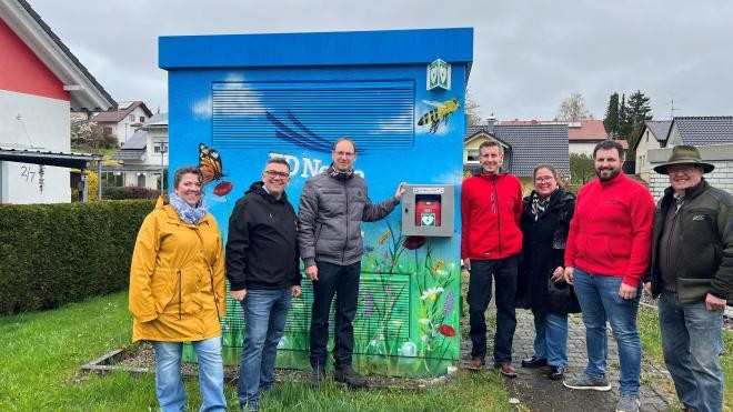 Von links nach rechts stehen vor dem bunt bemalten POP in der Schwarzwaldstraße Margrita Bahn, Mathias Schleicher, Bürgermeister Torben Dorn, Philipp Förg, Nicole Schill, Andreas Schlenker und Franz Schleicher (von links nach rechts) bei der Übergabe des Defibrillators.
