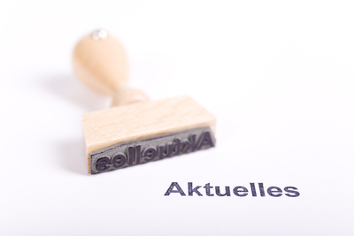 Liegender Holzstempel auf weißem Papier. Das Wort "Aktuelles" steht auf dem Papier.