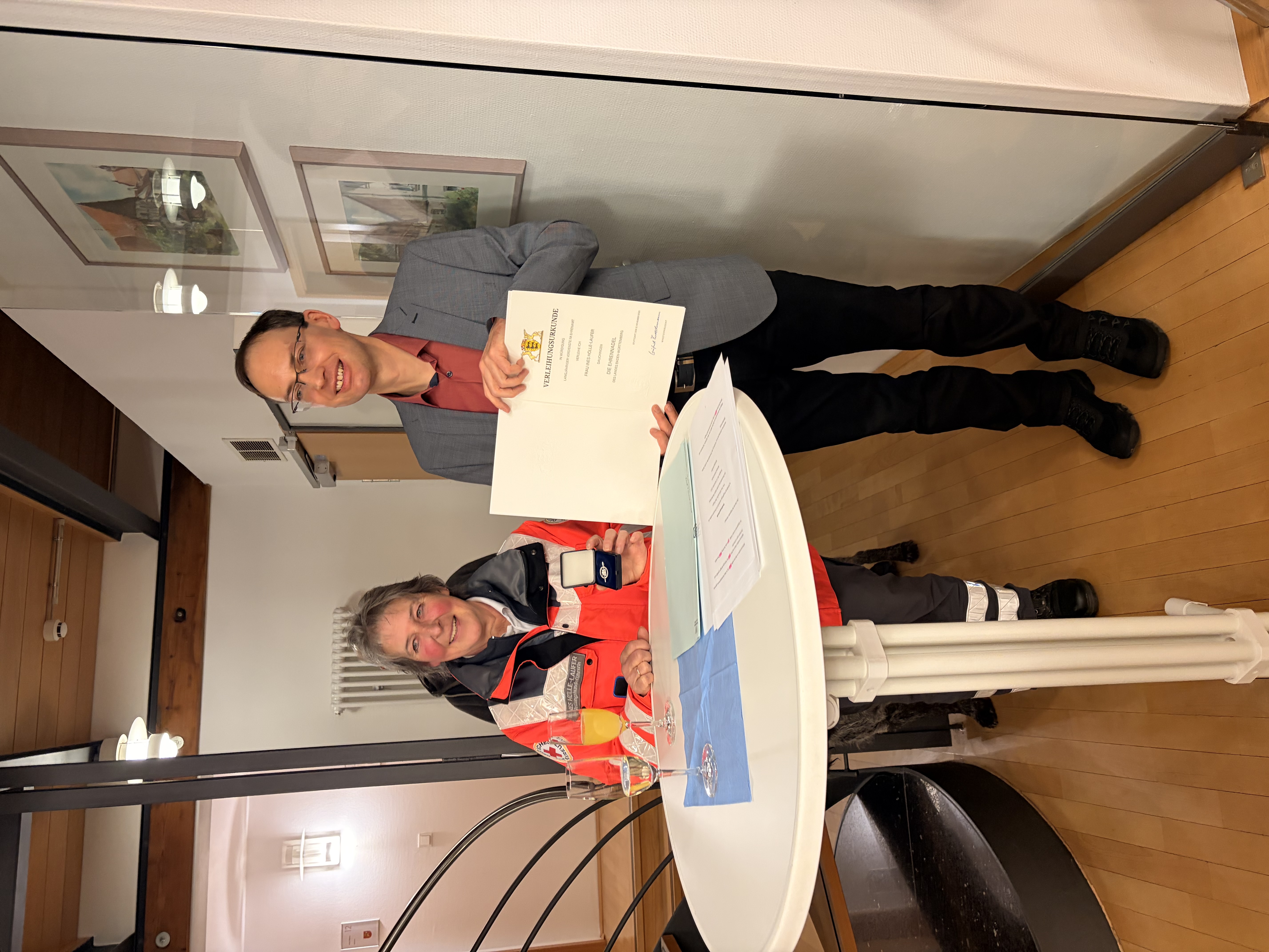 Links Frau Ines Hölle-Laufer vor einem Bistro-Stehtisch, rechts daneben Bürgermeister Torben Dorn mit der Urkunde in der Hand.