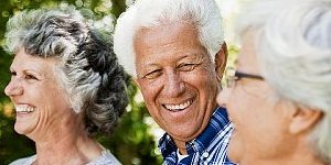 Drei ältere, lächelnde Menschen mit weißen Haaren im Freien.