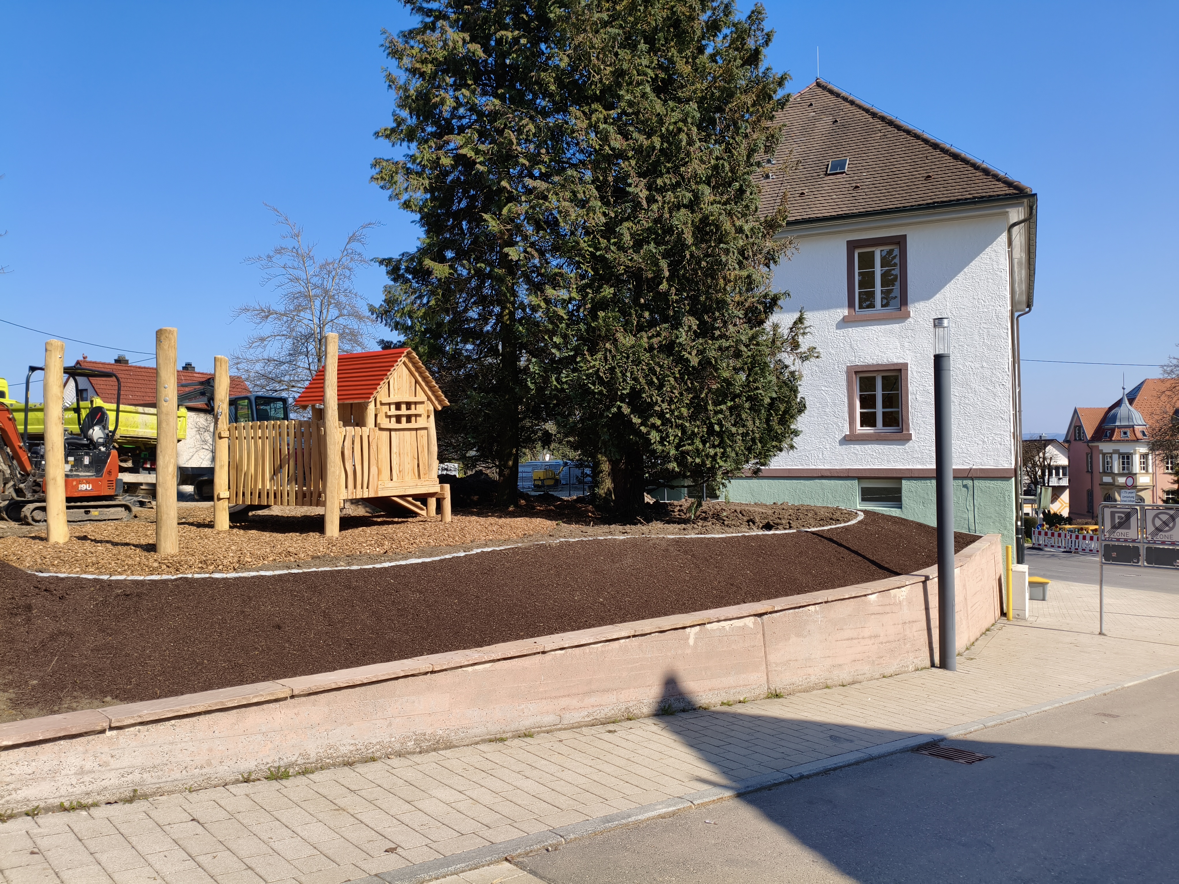 Ansicht von Straße. Angelegtes Beet, neue Spielgeräte und das Pfarrhaus.