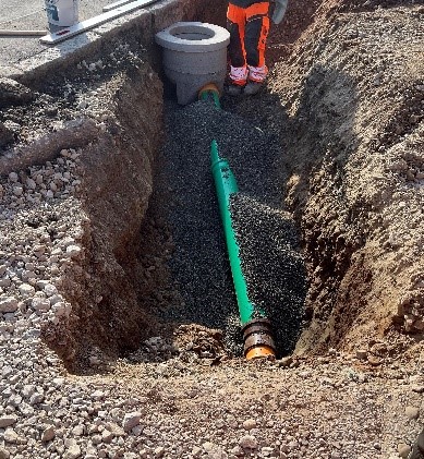 Offene Straße, grüner Schlauch in einer Grube.
