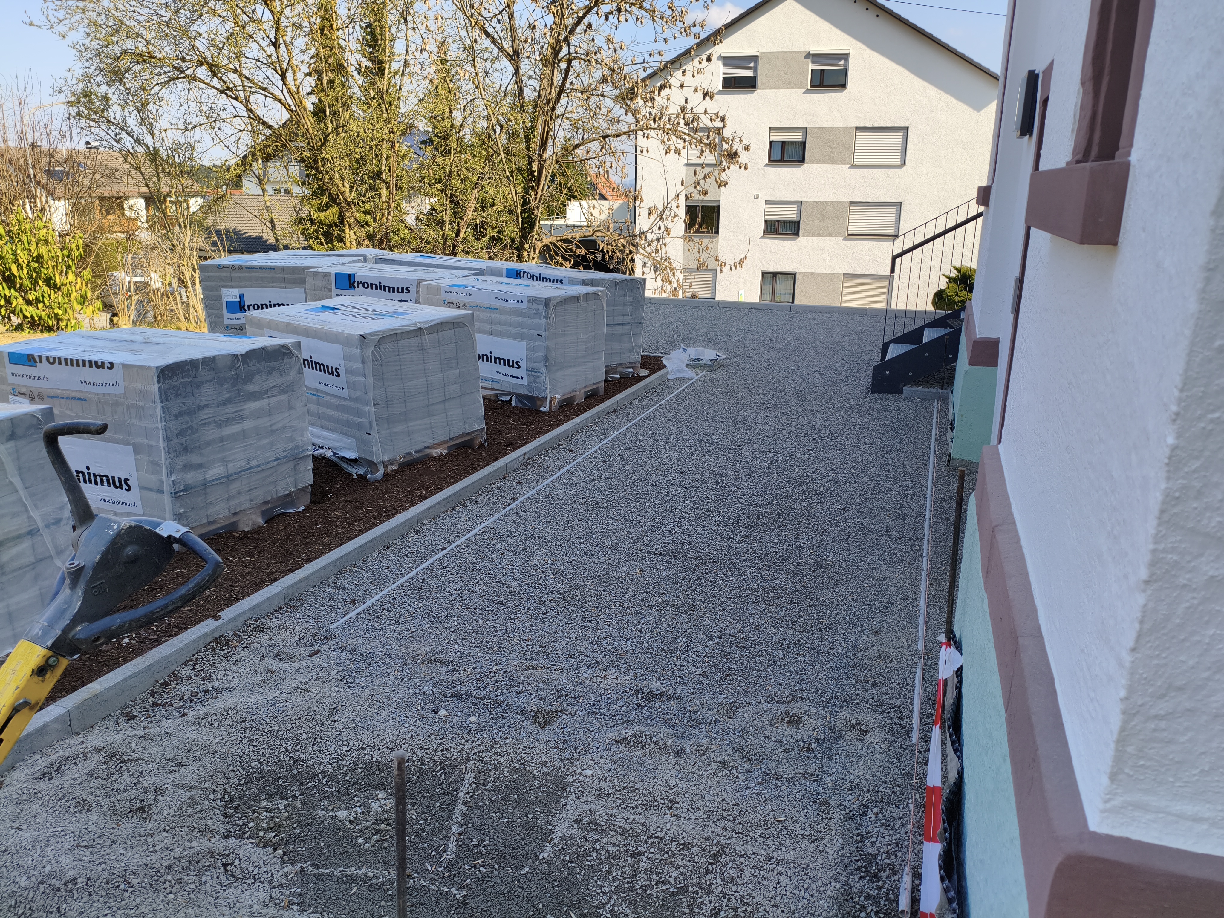 Ansicht im Eingangsbereich des Pfarrhauses. Kleine Schottersteine mit Randsteinen und Paletten mit Pflastersteinen.