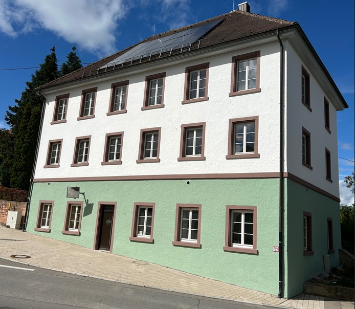 Das umgebaute Pfarrhaus mit seinem mintgrünen Sockel von der Straße aus fotografier.