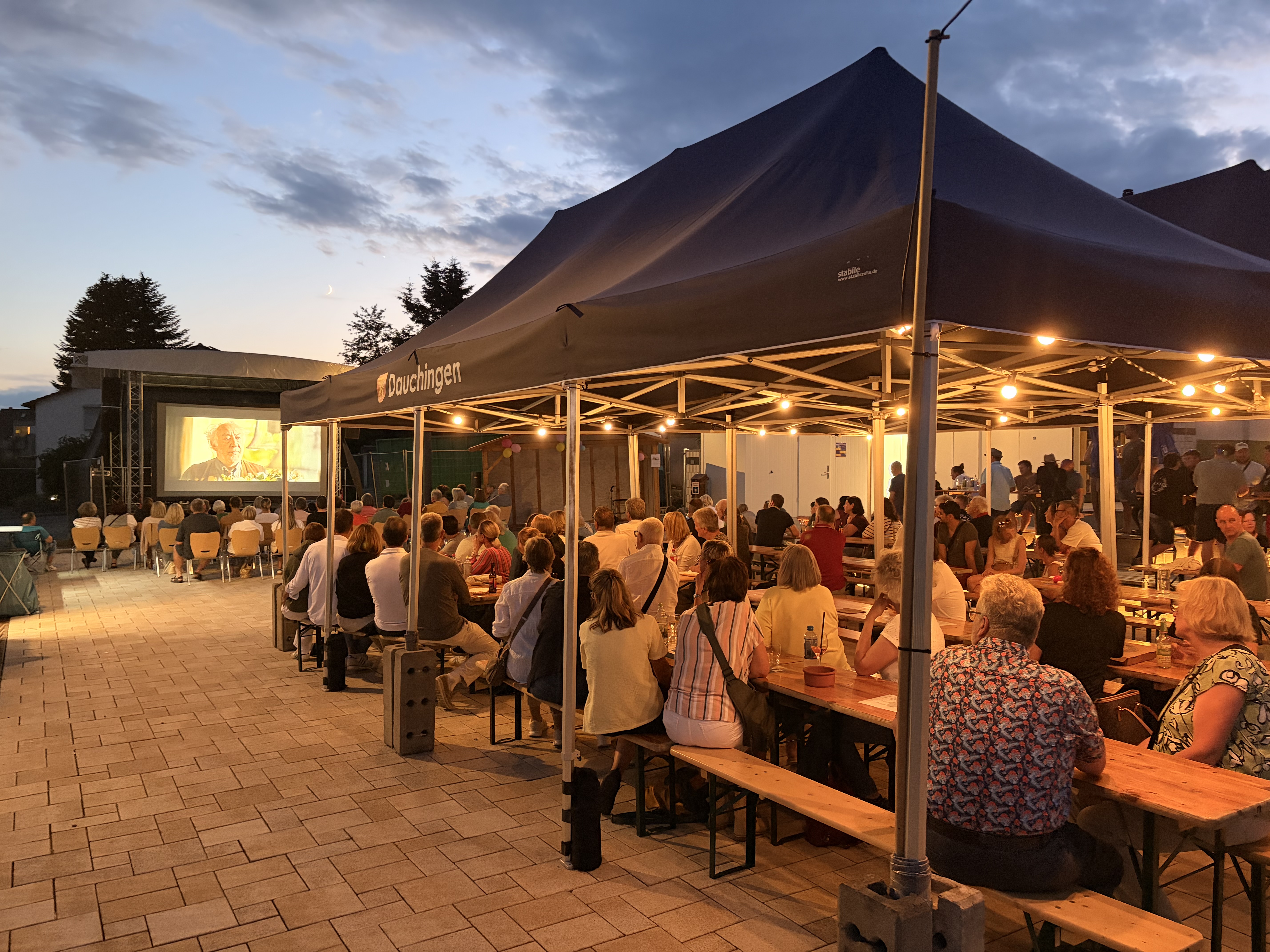 Die Besucher sitzen mit schöner Beleuchtung unter einem Zelt und schauen das Open-Air-Kino an-