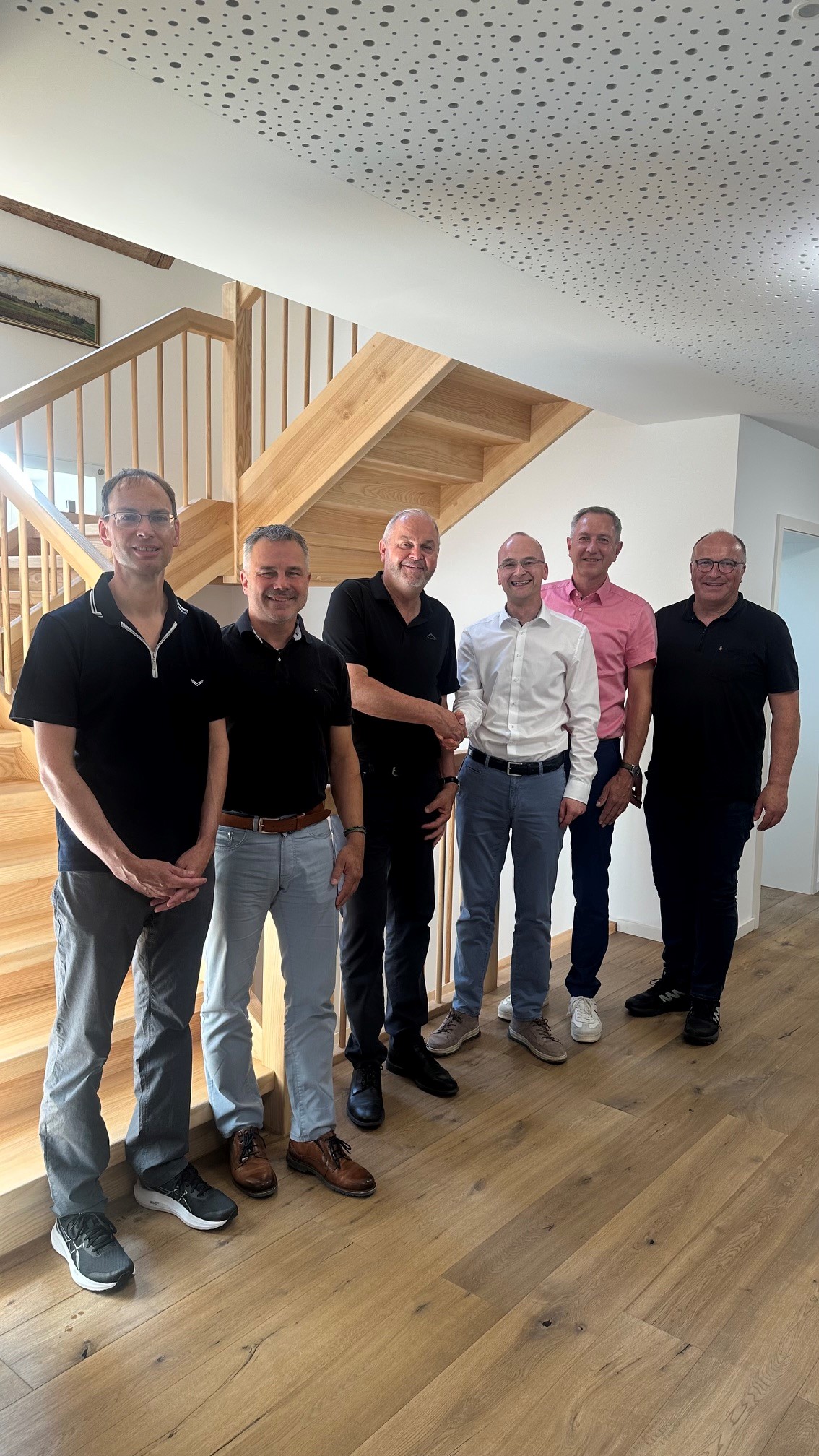 Die Herren Bürgermeister stehen vor einer Holztreppe und lächeln in die Kamera. Herr Fluck schüttelt die Hand von Herrn Ragg.